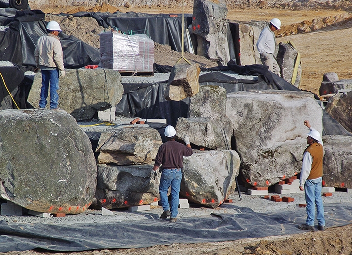 Construction of four large waterfall features is taking place above, with the larger boulders being set first. One thousand tons of select boulders were shipped from New York to Florida for this effort. These boulders sit on a fiber-reinforced concrete pad poured on top of the pond liner.