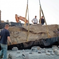 This large commercial entry waterfall weir rock is being set in place, and its position will be adjusted by using heavy-duty concrete blocks. Once the position is confirmed and adjacent boulders are set, concrete and rebar will be used to permanently secure them together.