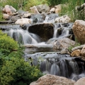 This cascading waterfall appears to initiate from a source higher up in the mountain, disappear, and then re-emerge close to the driveway.