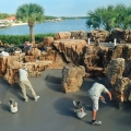 A black pebble plaster finish is being installed in front of the partially completed waterfall structure.
