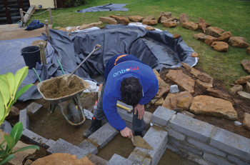 Constructing the 225-millimeter (9-inch) block wall to support the small stones within the stream/waterfall.